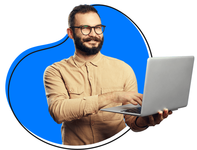 white man with a beard and glasses holding a laptop and smiling.