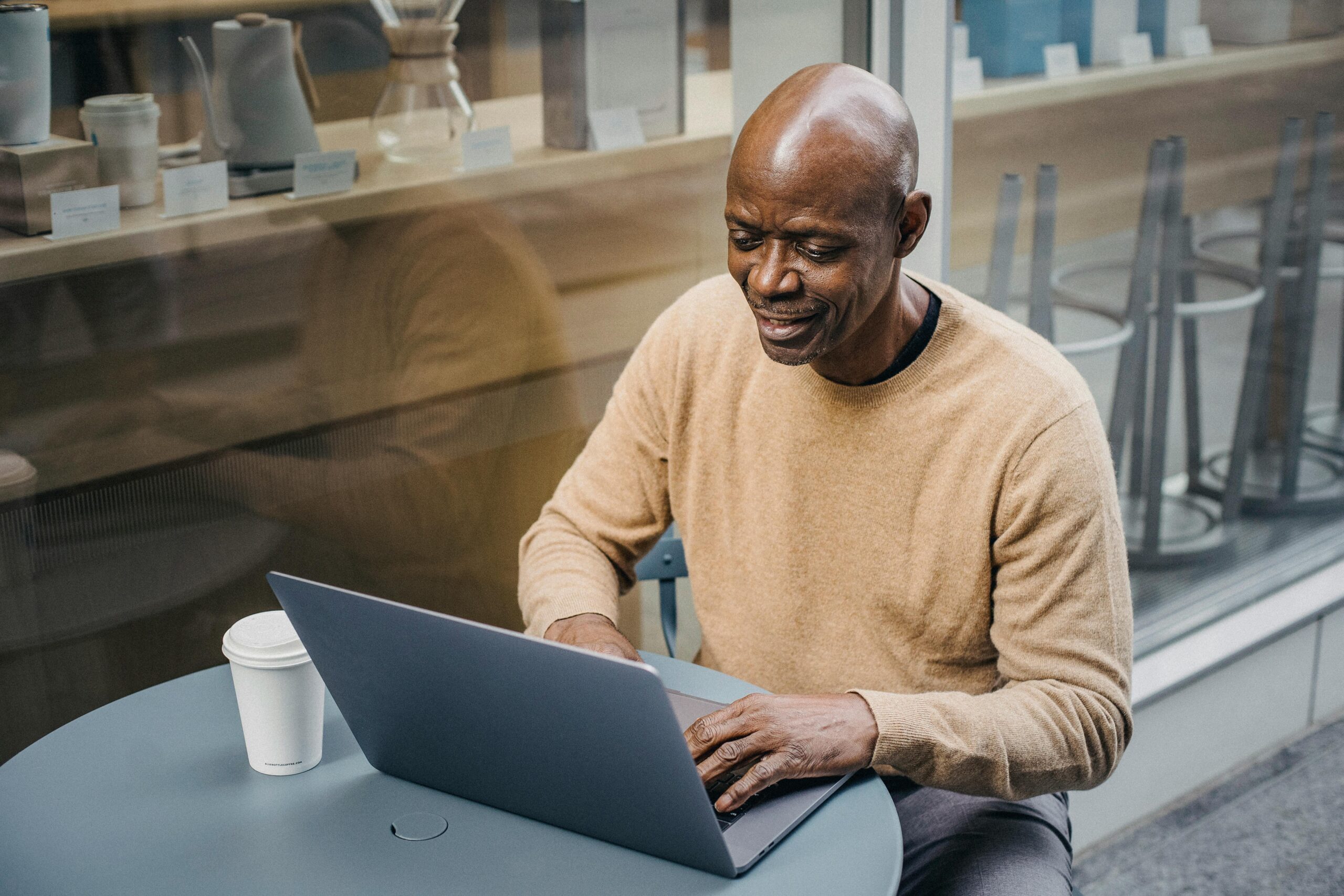 An man working on a laptop at a café table by the window.