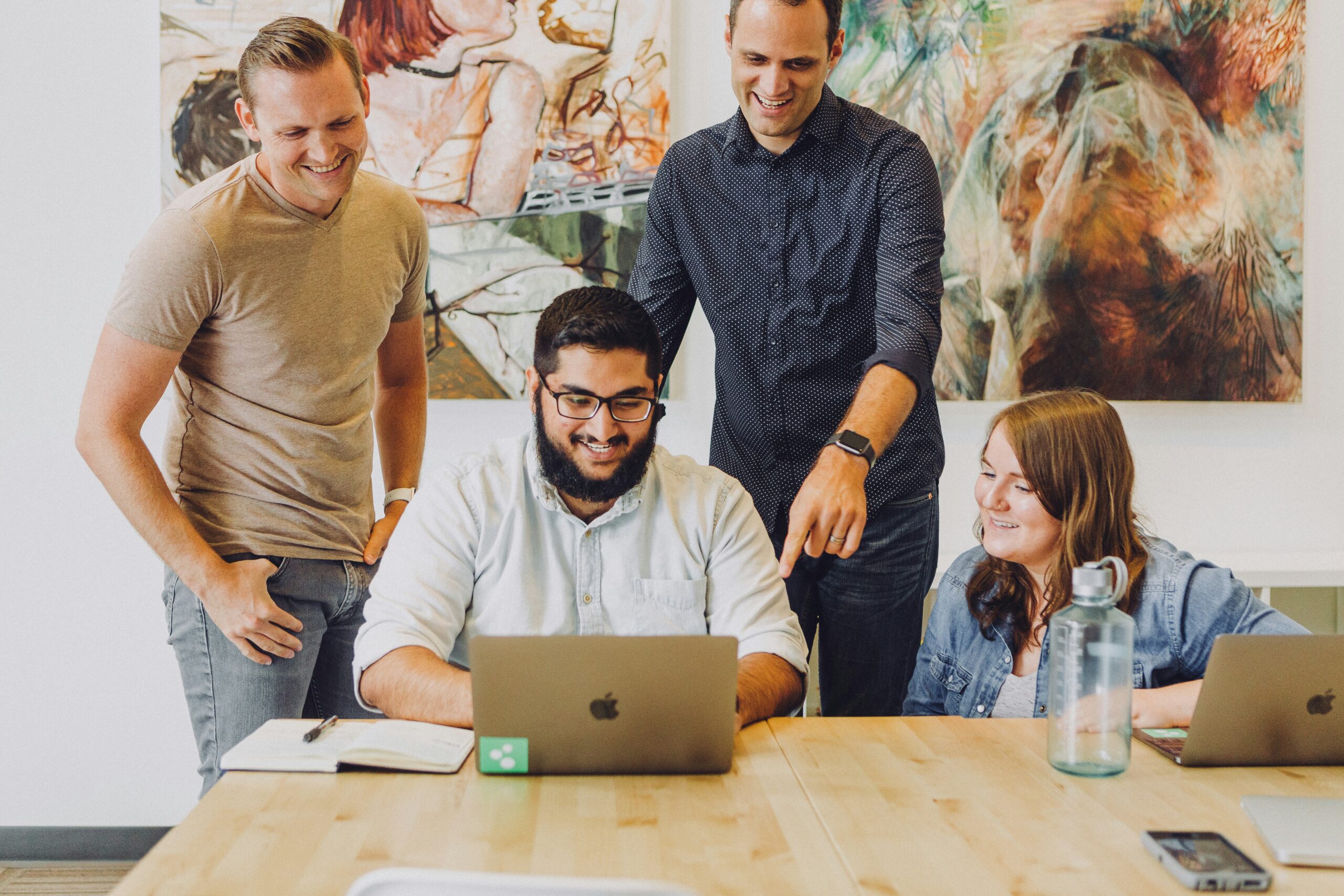 A group of four colleagues collaborating around a wooden table in a bright workspace.